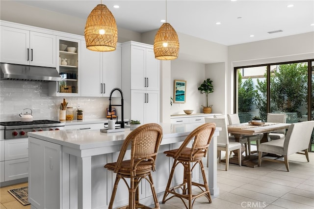 kitchen with under cabinet range hood, visible vents, backsplash, an island with sink, and stainless steel gas stovetop