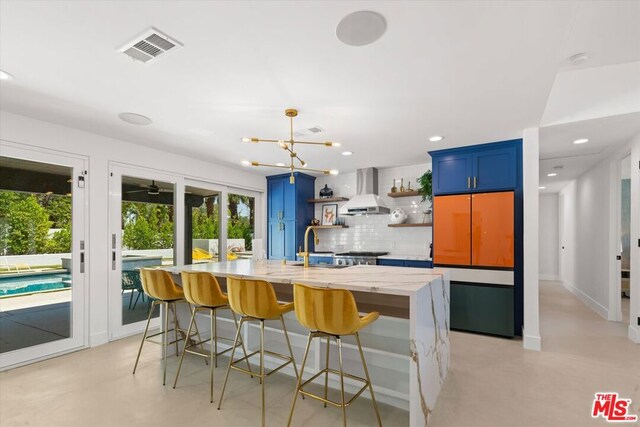 kitchen with tasteful backsplash, a breakfast bar, blue cabinets, and wall chimney exhaust hood