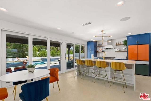 kitchen featuring blue cabinets, a kitchen bar, tasteful backsplash, wall chimney range hood, and pendant lighting