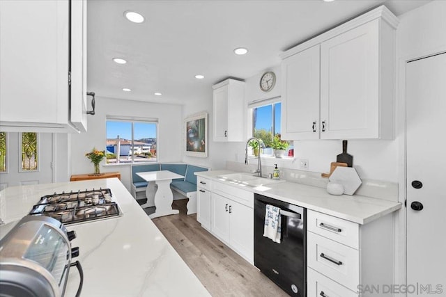 kitchen with sink, white cabinets, black dishwasher, and light stone countertops