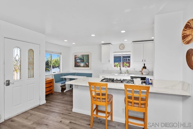 kitchen featuring sink, white cabinets, a kitchen bar, light hardwood / wood-style floors, and kitchen peninsula