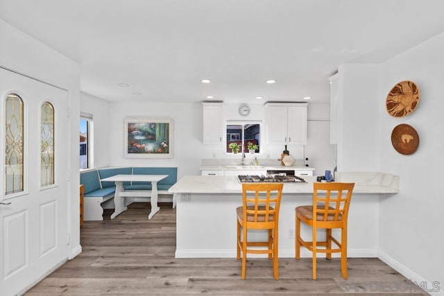 kitchen featuring white cabinets, a kitchen bar, light wood-type flooring, kitchen peninsula, and stainless steel gas stovetop