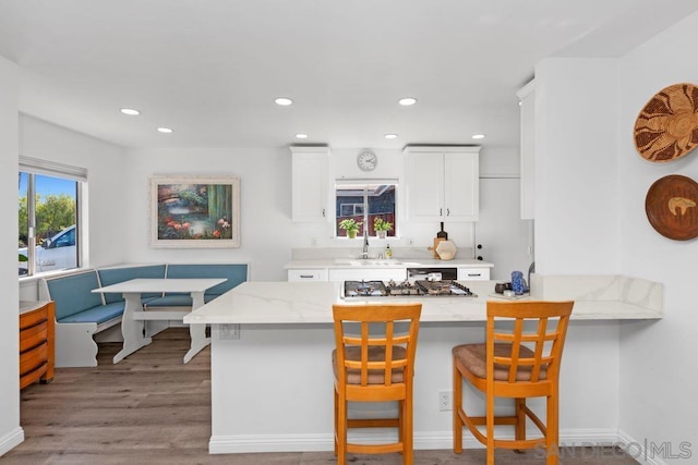 kitchen with white cabinets, light stone counters, light hardwood / wood-style flooring, kitchen peninsula, and a breakfast bar area