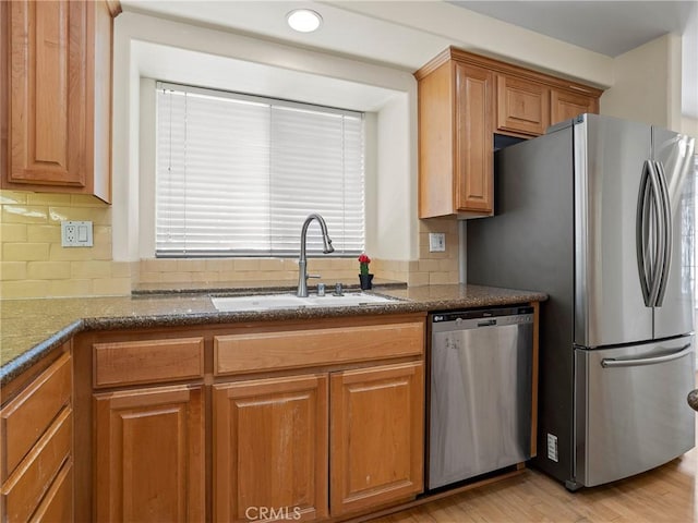 kitchen with dark stone countertops, stainless steel appliances, sink, light hardwood / wood-style flooring, and tasteful backsplash