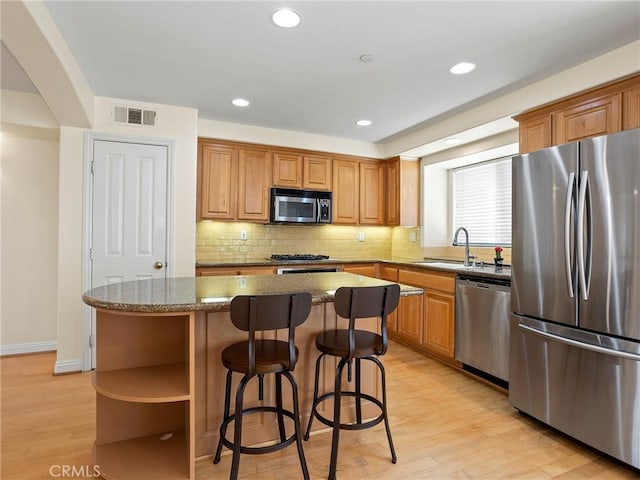 kitchen with stainless steel appliances, a center island, dark stone counters, sink, and light hardwood / wood-style flooring