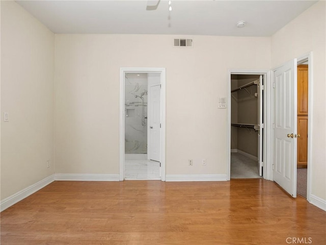 unfurnished bedroom with a spacious closet, a closet, light hardwood / wood-style floors, connected bathroom, and ceiling fan