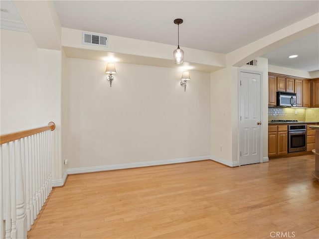 interior space featuring stainless steel appliances, decorative light fixtures, light wood-type flooring, and tasteful backsplash