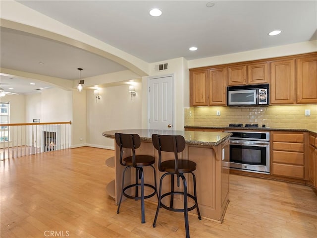 kitchen with pendant lighting, stainless steel appliances, a kitchen island, stone countertops, and ceiling fan