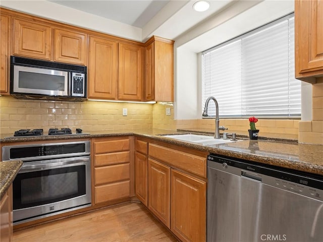 kitchen featuring tasteful backsplash, light wood-type flooring, dark stone counters, appliances with stainless steel finishes, and sink