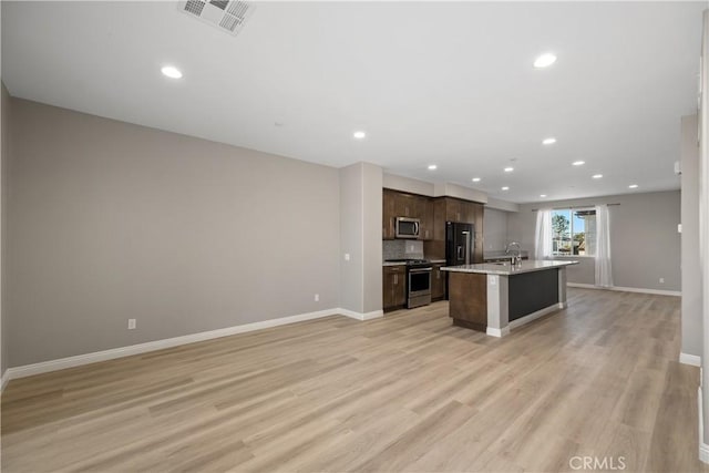 kitchen featuring sink, light hardwood / wood-style flooring, stainless steel appliances, dark brown cabinetry, and an island with sink