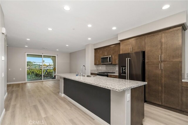 kitchen featuring tasteful backsplash, sink, a kitchen island with sink, stainless steel appliances, and light stone countertops