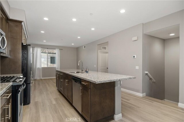 kitchen with sink, dark brown cabinets, light hardwood / wood-style flooring, appliances with stainless steel finishes, and a kitchen island with sink