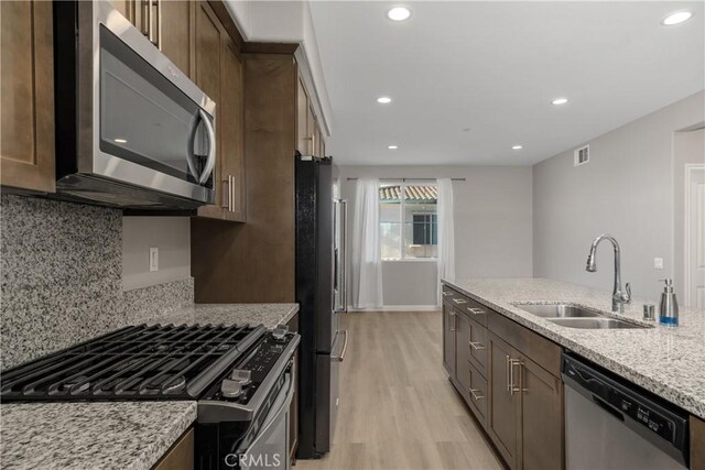 kitchen featuring sink, appliances with stainless steel finishes, light stone counters, tasteful backsplash, and light hardwood / wood-style floors