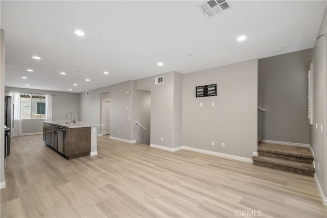 kitchen with dark brown cabinetry, sink, light wood-type flooring, and a center island with sink