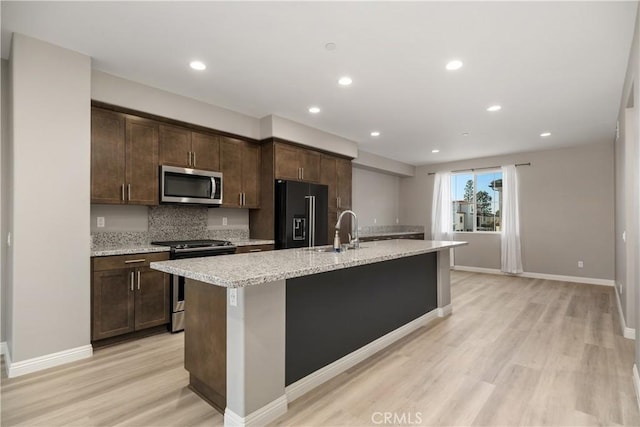 kitchen featuring light hardwood / wood-style flooring, a kitchen island with sink, backsplash, stainless steel appliances, and dark brown cabinetry