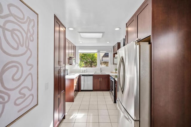 kitchen with sink, light tile patterned flooring, a skylight, and appliances with stainless steel finishes