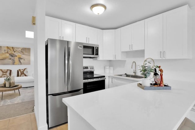 kitchen with sink, light tile patterned floors, stainless steel appliances, white cabinets, and kitchen peninsula