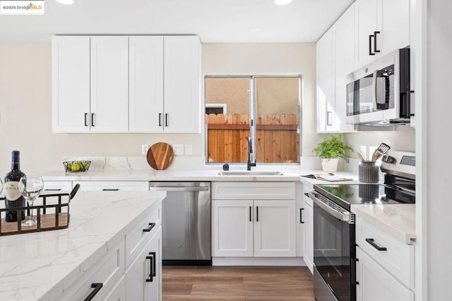 kitchen featuring appliances with stainless steel finishes, white cabinetry, light stone counters, and sink