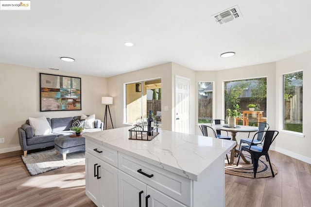 kitchen with light stone counters, light wood-type flooring, a healthy amount of sunlight, and white cabinetry