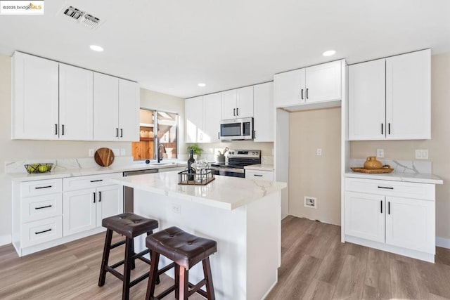 kitchen featuring stainless steel appliances, a center island, white cabinets, light hardwood / wood-style flooring, and sink