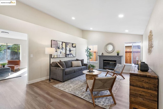 living room with high vaulted ceiling, a brick fireplace, and hardwood / wood-style flooring