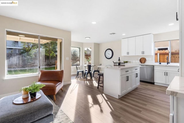 kitchen with dishwasher, a wealth of natural light, white cabinetry, wood-type flooring, and sink