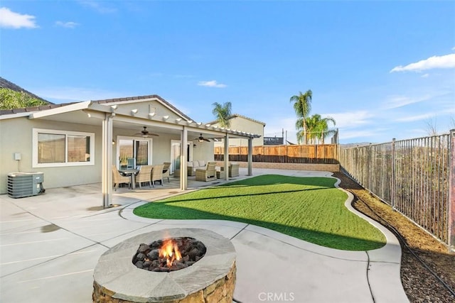 view of yard featuring ceiling fan, an outdoor living space with a fire pit, central air condition unit, and a patio area