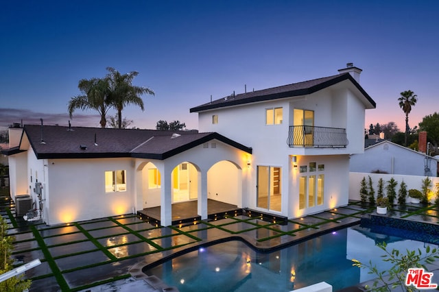 back house at dusk featuring a balcony, a patio, central AC, and a fenced in pool