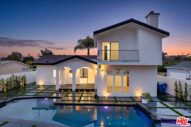 back house at dusk with a balcony, a patio, and a fenced in pool