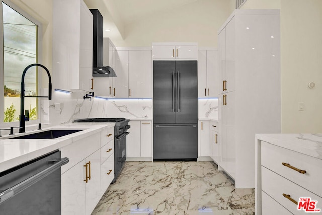 kitchen with high end appliances, sink, wall chimney exhaust hood, white cabinets, and tasteful backsplash