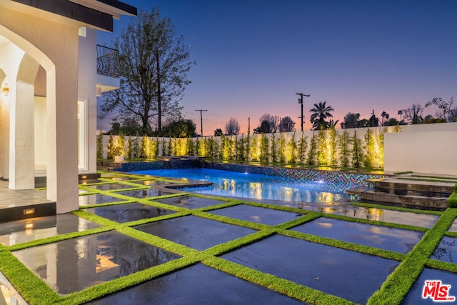 pool at dusk featuring pool water feature and a patio