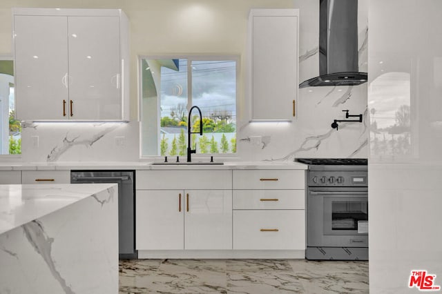 kitchen featuring stainless steel appliances, sink, white cabinets, light stone counters, and wall chimney exhaust hood