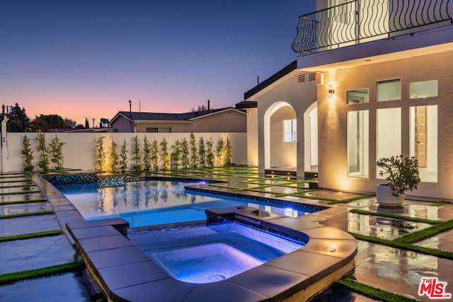 pool at dusk featuring a patio area and an in ground hot tub