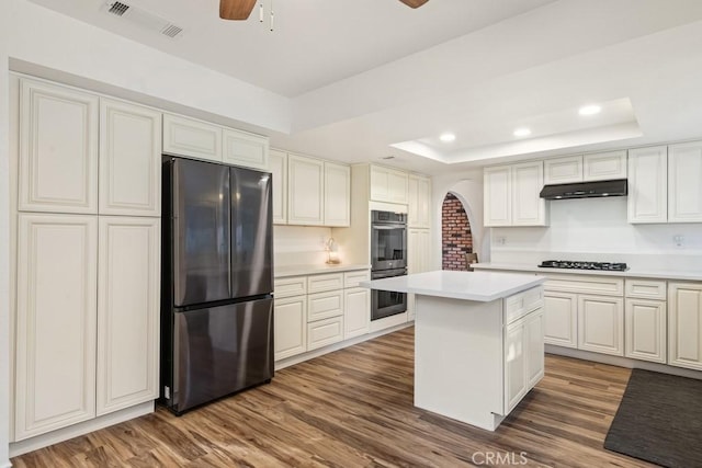 kitchen with gas stovetop, a kitchen island, double oven, a tray ceiling, and stainless steel refrigerator