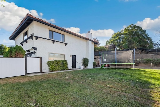 rear view of property featuring a yard and a trampoline