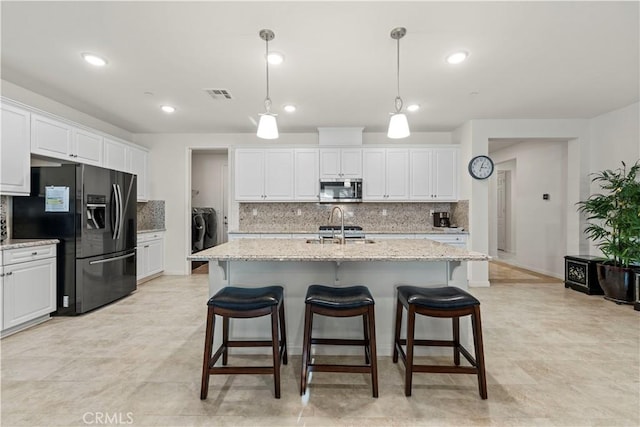 kitchen with hanging light fixtures, white cabinets, black refrigerator with ice dispenser, and a center island with sink