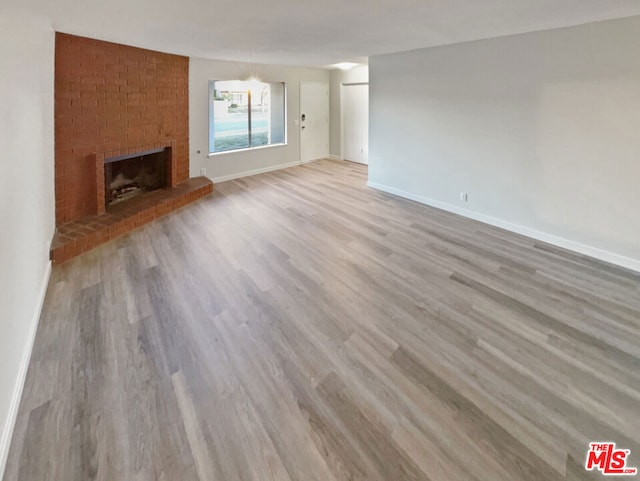 unfurnished living room with a brick fireplace and light wood-type flooring