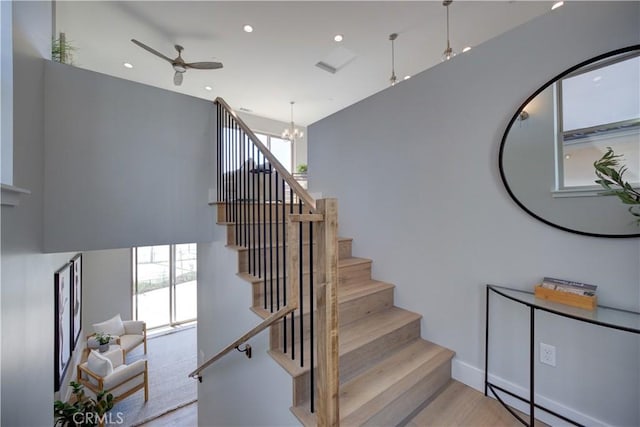 stairway with ceiling fan with notable chandelier, recessed lighting, baseboards, and wood finished floors