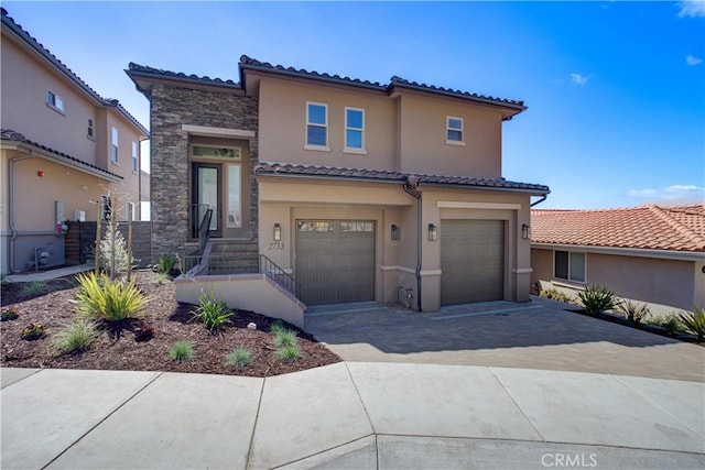 mediterranean / spanish house featuring a garage, driveway, stone siding, and stucco siding