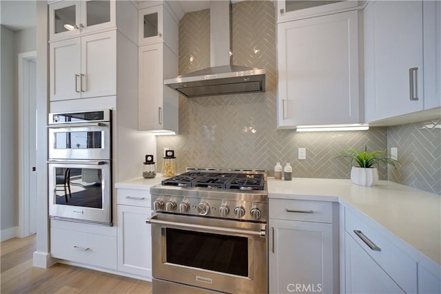 kitchen featuring stainless steel appliances, light countertops, backsplash, white cabinets, and wall chimney exhaust hood