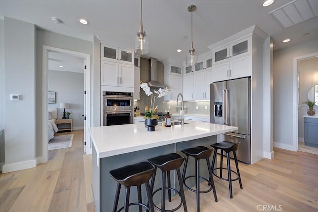 kitchen with tasteful backsplash, wall chimney exhaust hood, appliances with stainless steel finishes, light wood-type flooring, and a sink