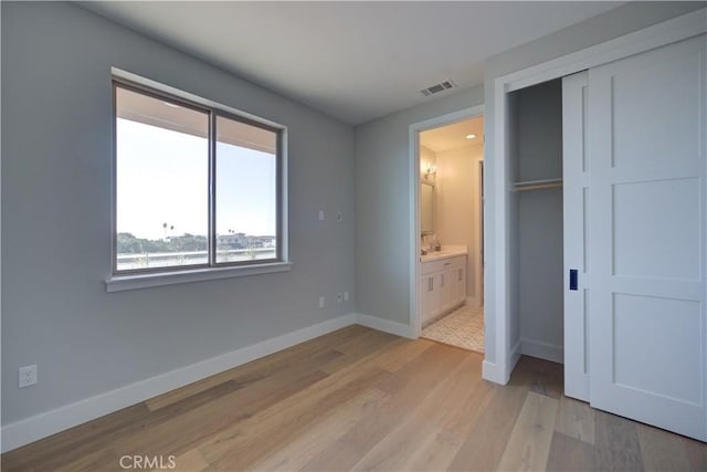 unfurnished bedroom with visible vents, baseboards, light wood-style floors, a closet, and ensuite bath