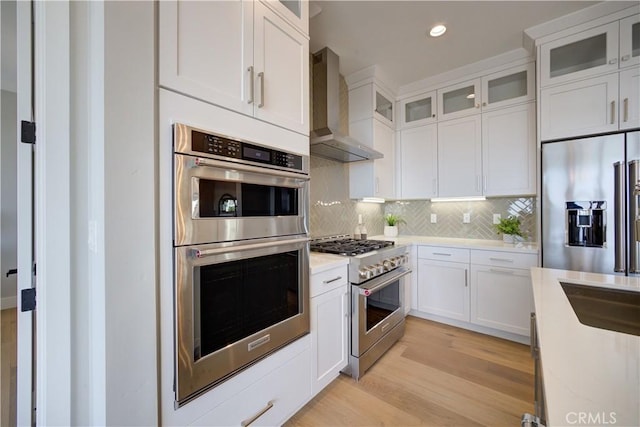 kitchen featuring wall chimney range hood, light wood-type flooring, high quality appliances, and white cabinetry