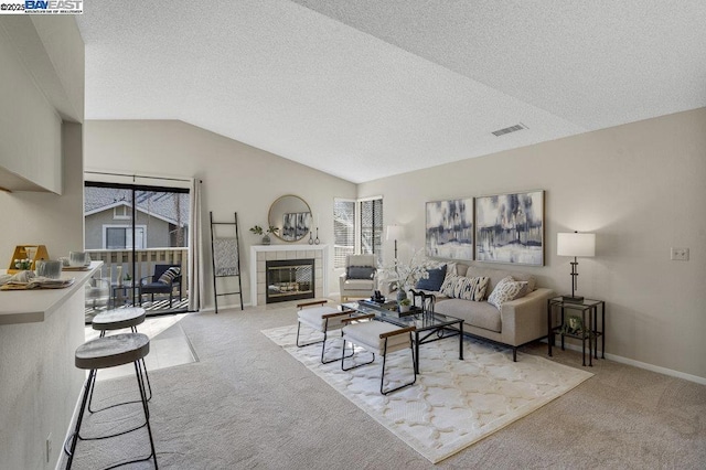 living room featuring a tile fireplace, light colored carpet, vaulted ceiling, and a textured ceiling