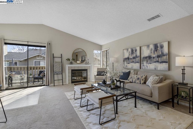 carpeted living room featuring a textured ceiling, a tile fireplace, and vaulted ceiling