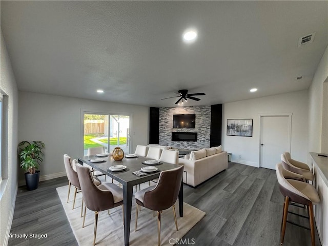 dining room featuring a stone fireplace, ceiling fan, and dark hardwood / wood-style floors