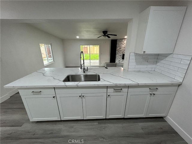 kitchen with white cabinets, kitchen peninsula, light stone counters, and sink