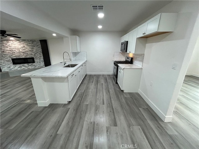 kitchen with stainless steel gas stove, kitchen peninsula, ceiling fan, sink, and white cabinetry