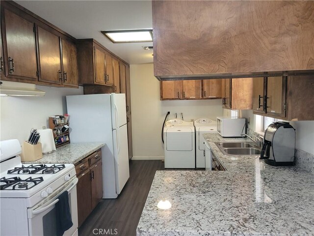 kitchen featuring under cabinet range hood, white appliances, a sink, washer and dryer, and dark wood-style floors