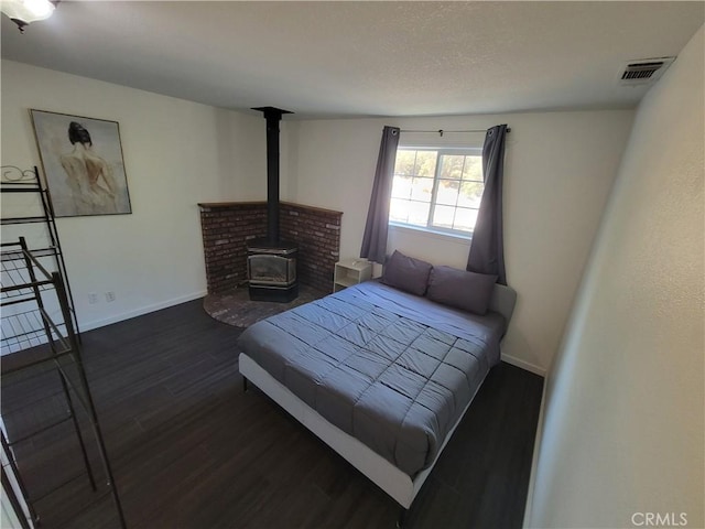 bedroom with dark wood-style floors, a wood stove, visible vents, and baseboards